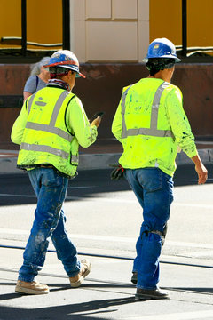 Two construction workers wearing their hard-hats and high viz vests walk back to their jobs on a downtown project in Tucson AZ