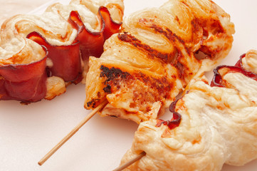 Pastry with fried bacon on sticks on white