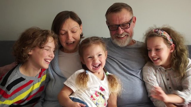 Portrait of a happy family of five on the sofa at home. Grandfather, grandmother and three grandchildren posing and looking at the camera