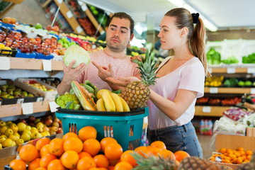 Cheerful family couple standing with full grocery cart after shopping