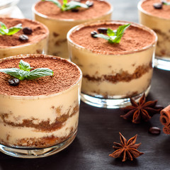 classical tiramisu dessert in a glass sprinkled with cocoa and decorated with coffee beans on a dark background, luxury dessert