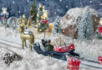 Sled loaded of gifts and miniature car carrying a christmas tree on snowy landscape