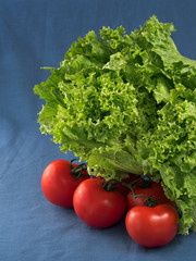 Green salad and fresh tomatoes on a blue textile background, close-up. Selective focus on lettuce leaves. Vertical orientation. Fresh green vegetables.