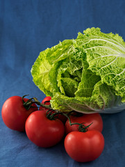 Chinese cabbage and fresh tomatoes on a blue textile background, close-up. Selective focus on the leaves of cabbage. Vertical orientation.