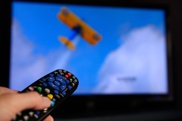 Man pointing a universal remote control towards a television screen to change the program