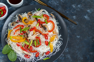 Oriental rice noodles Udon with sweet pepper, mushrooms. On a dark background.