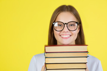 beautiful young woman in a white shirt on a yellow background in glasses with books in her hands