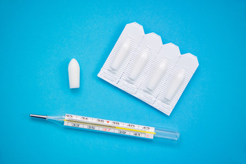 White suppositories for anal or vaginal use on blue background and a thermometer with temperature...