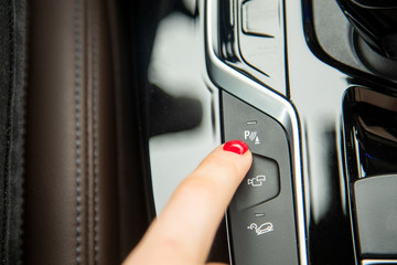 Obraz premium the finger of a female hand points to the parking assistant button, the equipment of a modern car. close-up, soft focus, blur background