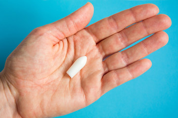 White suppository for anal or vaginal use in patient's hand on blue background. Medical candles for the treatment of Candida, thrush, hemorrhoids, inflammation and fever. Effective drug. Copy space