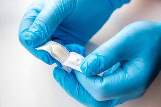 A gloved doctor opens suppositories for anal or vaginal use. Medical candles for the treatment of Candida, thrush, hemorrhoids, inflammation and fever. Effective drug on a white background