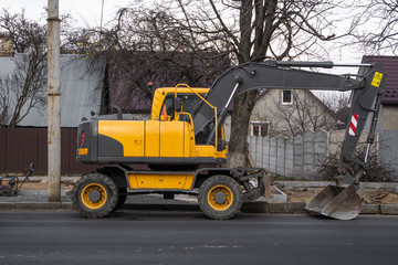 Yellow excavator standing on a road on construction site of the road on a street. Heavy industry. Construction of a road.