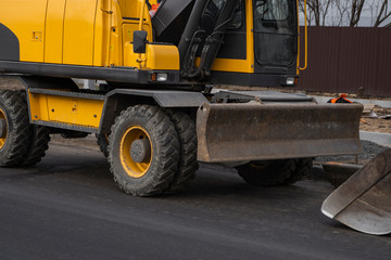 Yellow excavator standing on a road on construction site of the road on a street. Heavy industry. Construction of a road.