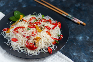 Oriental rice noodles Udon with sweet pepper, mushrooms. On a dark background.