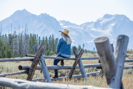 Woman sitting on wooden fence by mountains in Stanley, Idaho, USA