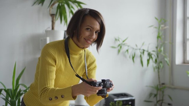 Tilt up of professional female photographer arranging objects on table and taking Christmas flatlay images with camera in office, then looking at camera and smiling