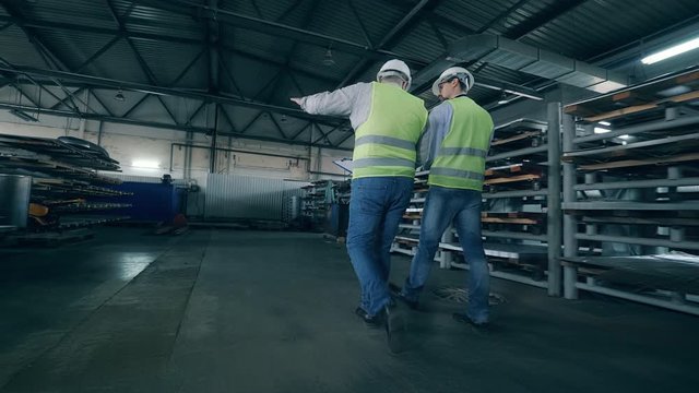 Two male workers are walking along factory premises