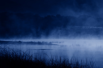 Early morning or night fog over the lake. Landscape in trendy blue tones. Color of the year 2020, Classic Blue.