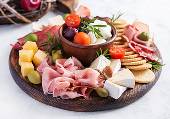 Antipasto platter with ham, prosciutto, salami, cheese,  crackers and olives on a light background....