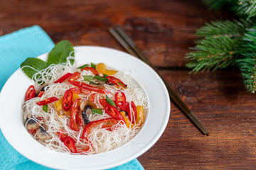 Oriental rice noodles Udon with sweet pepper, mushrooms. On a wooden background.