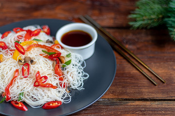 Oriental rice noodles Udon with sweet pepper, mushrooms. On a wooden background.