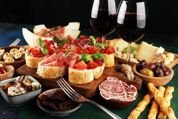Italian antipasti wine snacks set. Cheese variety, Mediterranean olives, seafood salad, Prosciutto di Parma, tomatoes, anchovy and wine in glasses