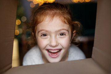 A happy child peeps into a gift box in and laughs. Concept of holidays, merry christmas and family.