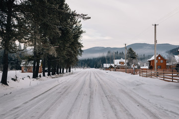 Photo of a forest road in the snow, near the house, a view of the mountains