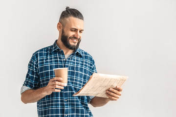 Freestyle. Guy in checkered shirt standing isolated on white reading newspaper drinking hot coffee smiling joyful copy space