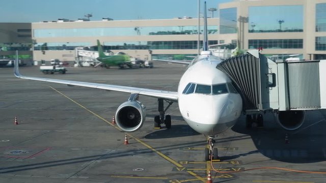 Plane is parked at the airport near the terminal. There is a boarding on the flight, people go through the tunnel into the aircraft. Airport buildings and other planes in the background. Close-up. 4K