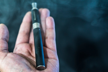 electronic cigarette or vaporizer in hand on black background