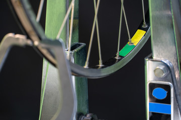 Fototapeta na wymiar Bicycle repair. The front wheel is on a stand on a black background. Rim and spokes close-up. Mechanic levels the wheel in the workshop. wheel truing stand