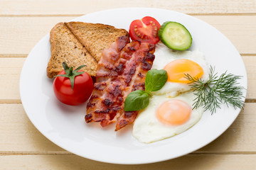 Fried eggs with bacon on the wooden table.