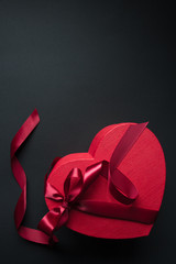 Red gift box heart shape with red ribbon on a black background, gift concept