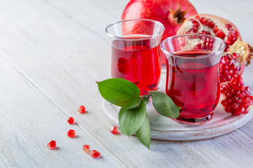 Two glasses of pomegranate juice and ripe pomegranate on a white wooden background. Healthy drink concept
