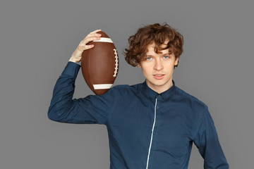 Sporty Lifestyle. Teenager boy standing isolated on grey with american football ball smiling playful