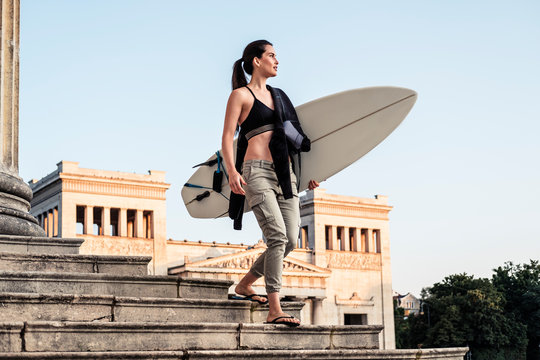 Young woman with surfboard on the way to Eisbach, Munich, Germany