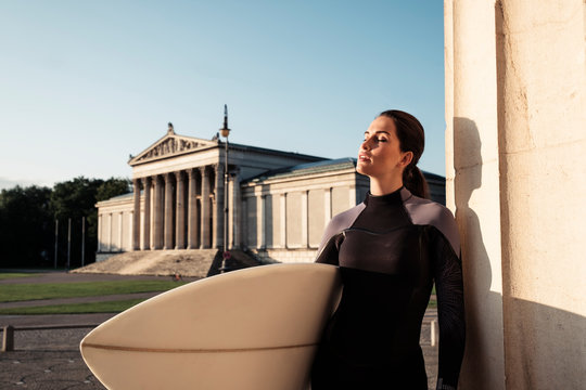 Portrait of young woman with surfboard relaxing at sunlight, Munich, Germany