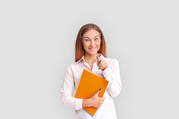 Freestyle. Young businesswoman standing isolated on white with notebook pointing at camera smiling cheerful