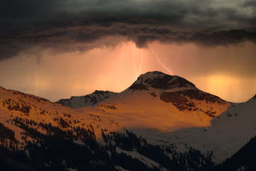 Fototapeta premium schneebedeckte Berge mit Gewitterwolken und Blitz