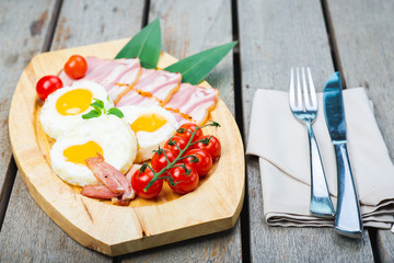 Tasty fried eggs with vegetables on a wooden plate.