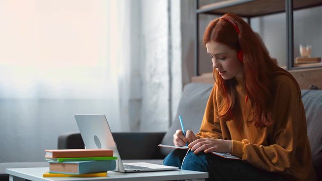 positive teenage girl in headphones doing homework