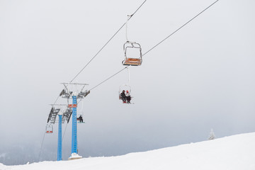 Chairlift moving in foggy and snowy day. Snow covered trees on the hills surrounding.