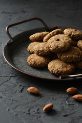 Gluten free vegan cookies concept. Almond bites in vintage tray and whole almond nuts on black background side view low key still life