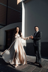 Happy to be together. Beautiful couple holding hands while walking through the city street. Young happy smiling beautiful plus size model in dress outdoors, xxl woman. Handsome guy in stylish suit.
