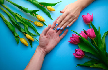 Holding hands on blue background with tulips, topdown view, holidays concept