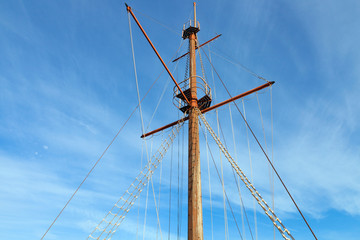 Wooden top of the old sailing ship mast, yards and rigging against blue sky . - 309270584