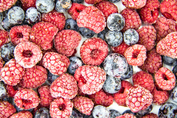 A Berry mix from frozen raspberries and blueberries. A Frozen Berries from freezer.  A sweet background with frozen raspberries and blueberries.   A heathy Berries in the background.