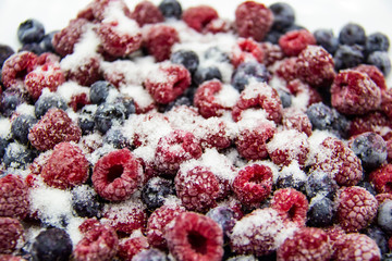 A Berry mix in sugar from frozen raspberries and blueberries. A Frozen Berries with Sugar.  A sweet background with frozen raspberries and blueberries. Sugar Berries in the background.  A heathy berry