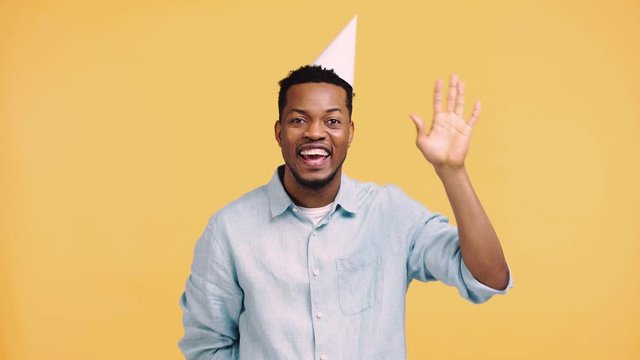 happy african american man waving hand isolated on yellow